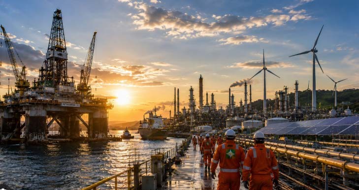 Equipe com EPIs caminhando em instalação industrial e offshore ao pôr do sol